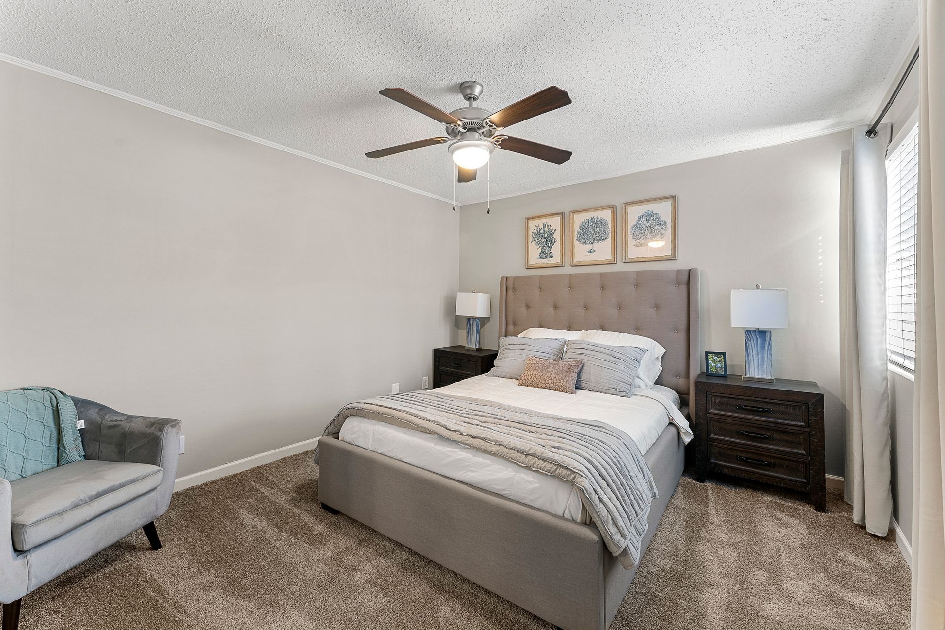 Bright bedroom with a bed, armchair, dresser, lamp, and ceiling fan