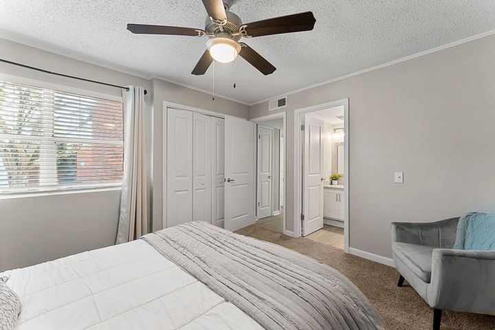 Bright bedroom with ceiling fan, white closet doors, window blinds, and gray chair.
