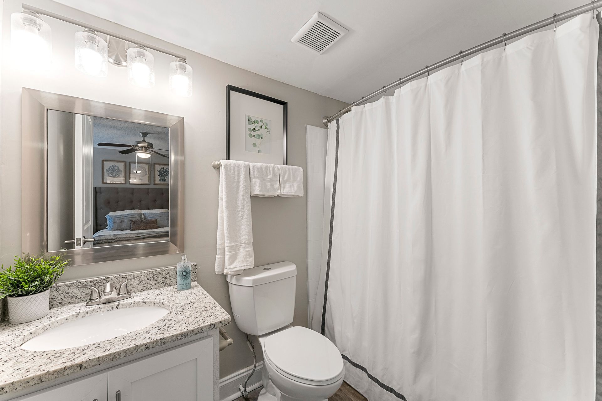 Bright bathroom with white shower curtain, toilet, vanity sink, and wall mirror.