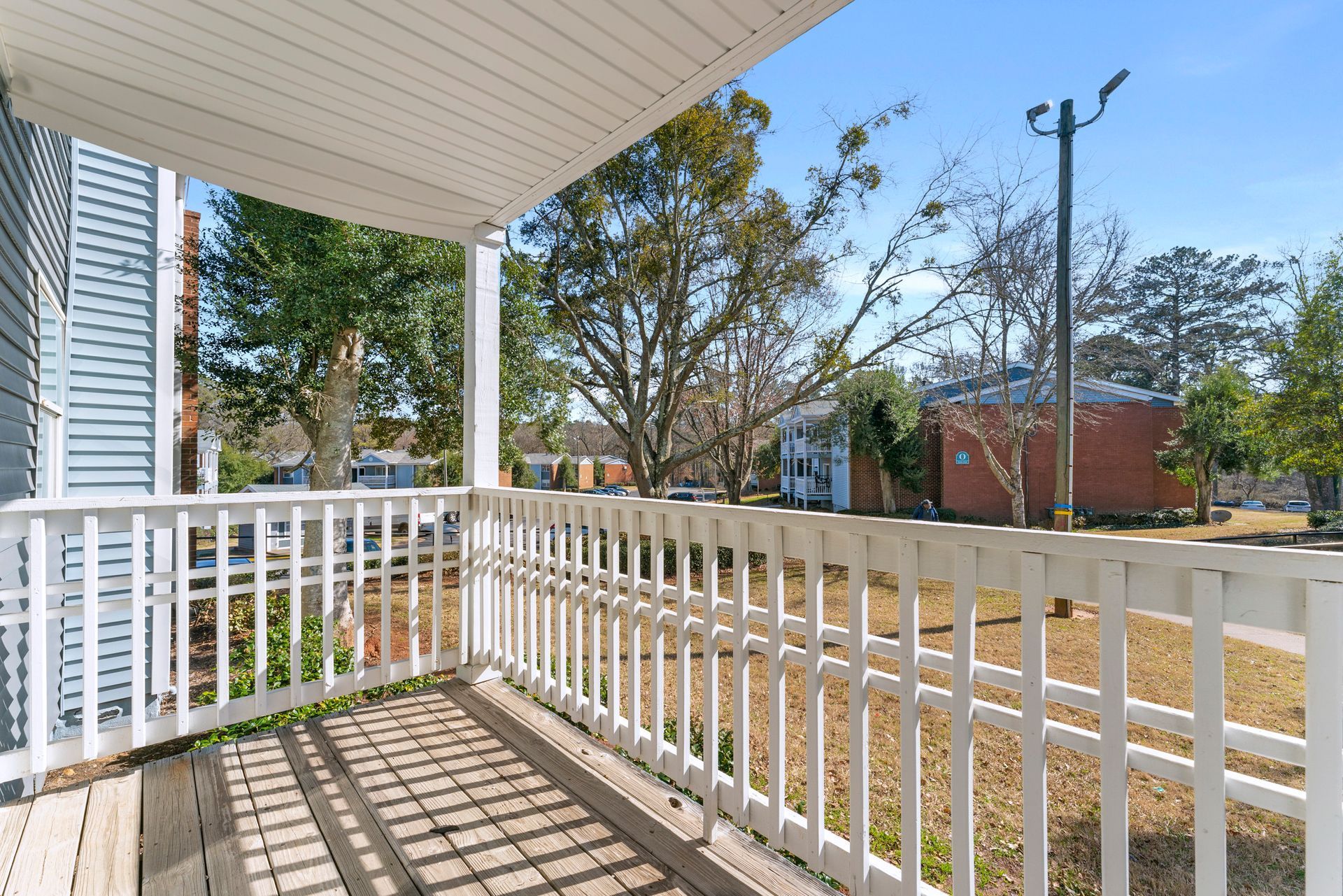 Front porch with white railing overlooking a tree-lined street on a sunny day