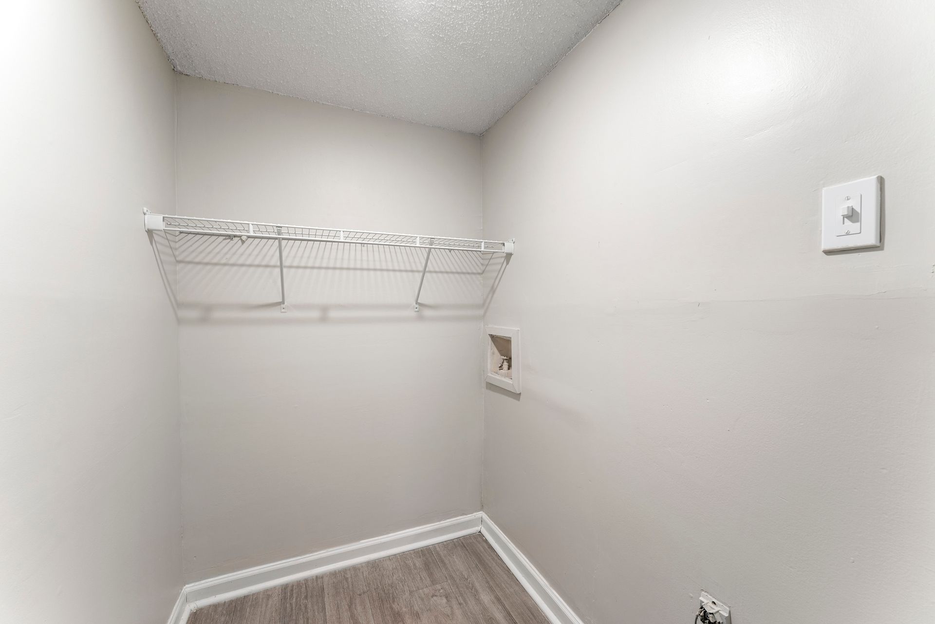 Empty walk-in closet with white walls, wire shelf, and wood-look floor.