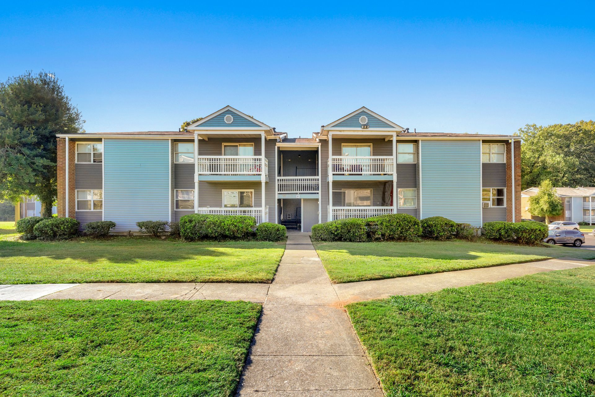 Apartment building with blue siding, central walkway, and green lawn under a clear sky