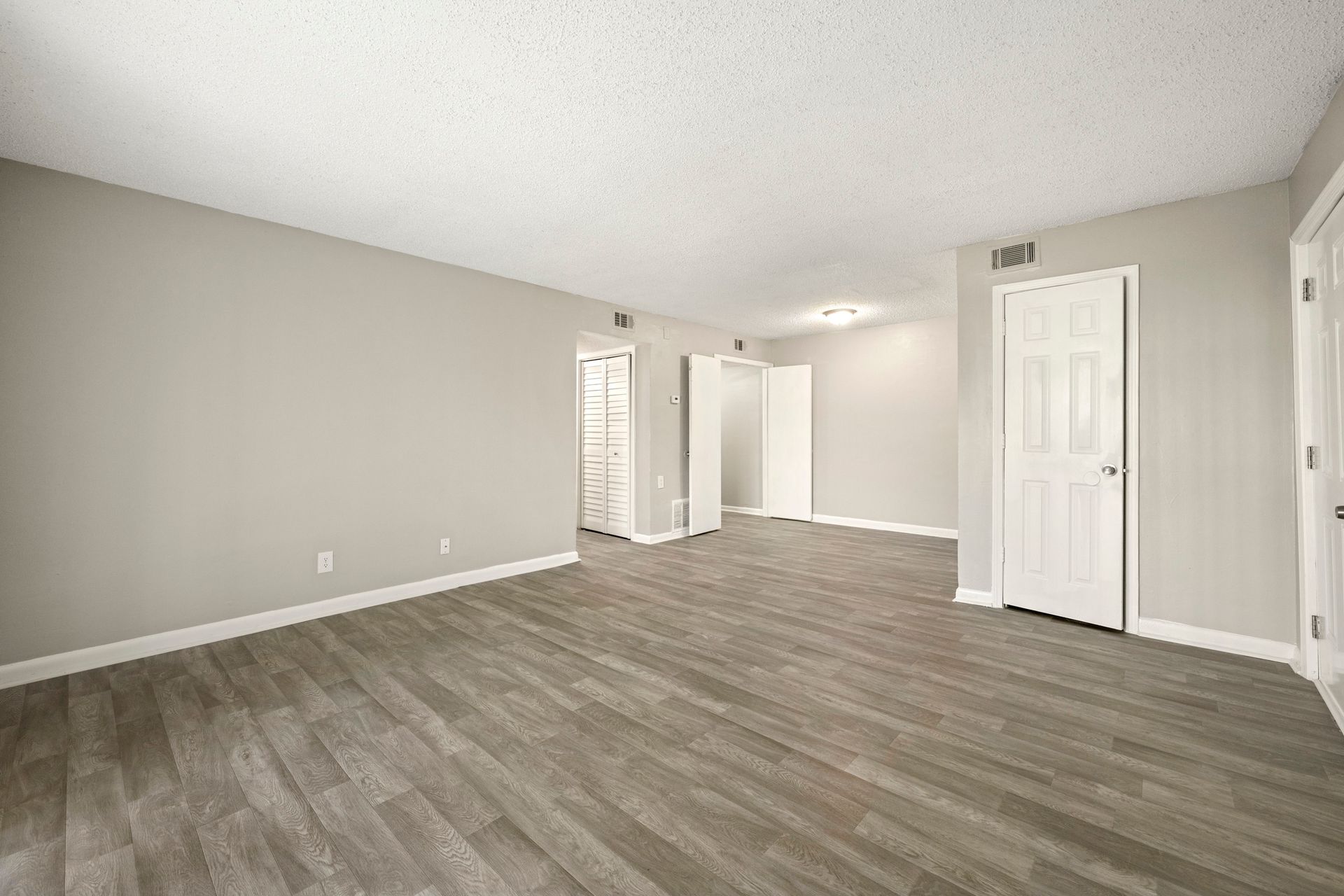 Empty gray living room with wood-look flooring, white doors, and sloped ceiling