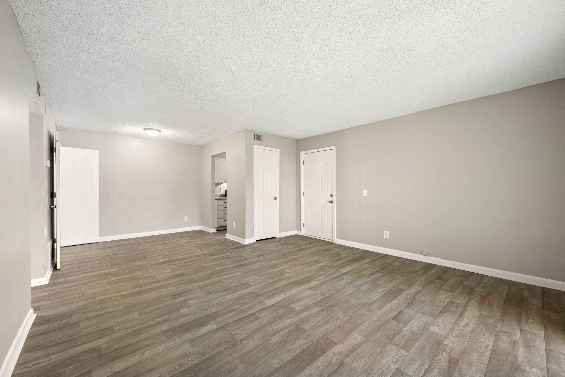 Empty beige room with wood-look flooring, white doors, and recessed ceiling lights