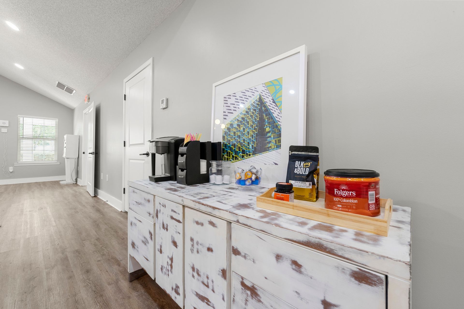 Bright hallway with a white cabinet holding coffee items, snacks, and a colorful framed print.