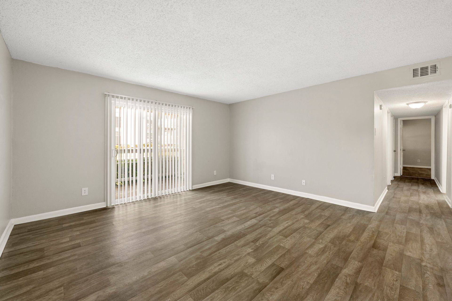 Empty gray living room with wood flooring and sliding glass door to the left.