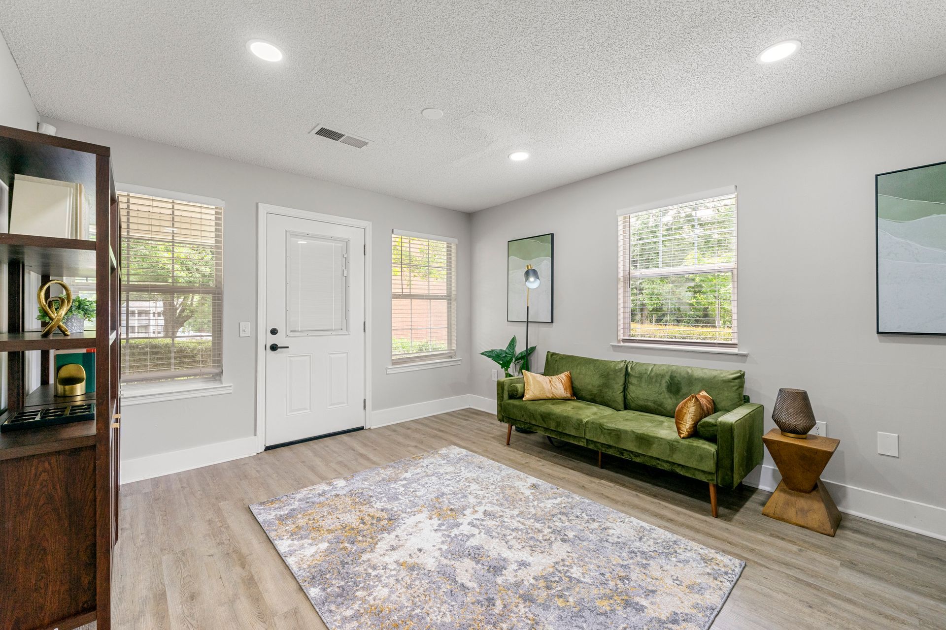 Bright living room with green sofa, patterned rug, windows, and white walls near a front door