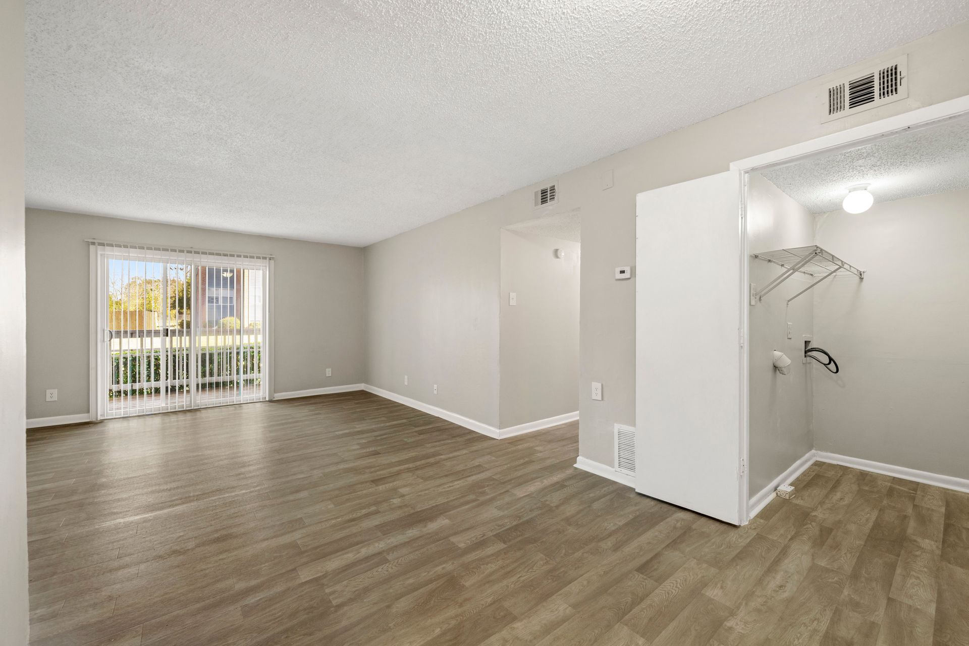 Empty living room with wood-look floors, sliding glass door, and open closet nook with white shelving