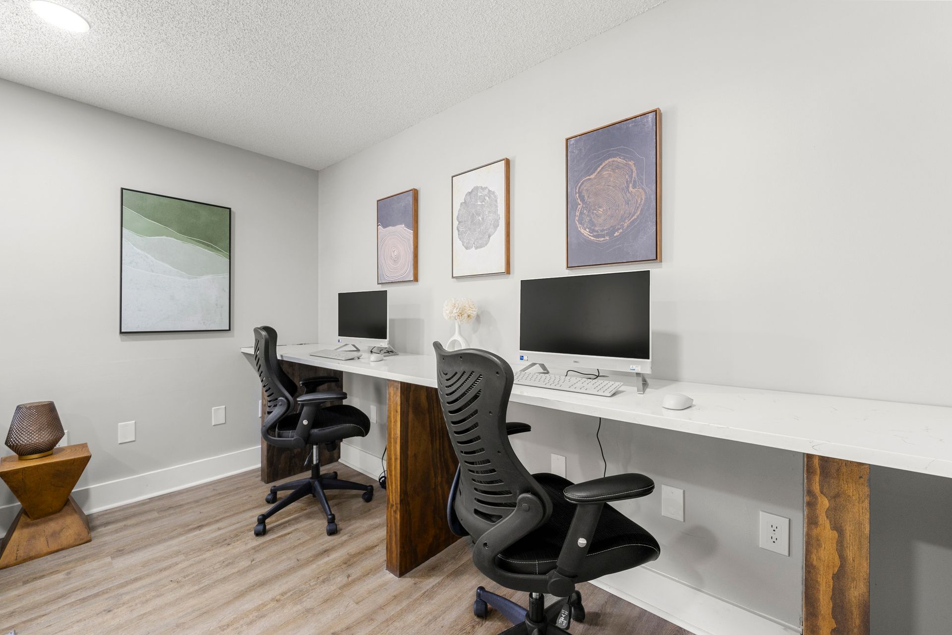 Modern home office with two black chairs, dual monitors, and framed wall art