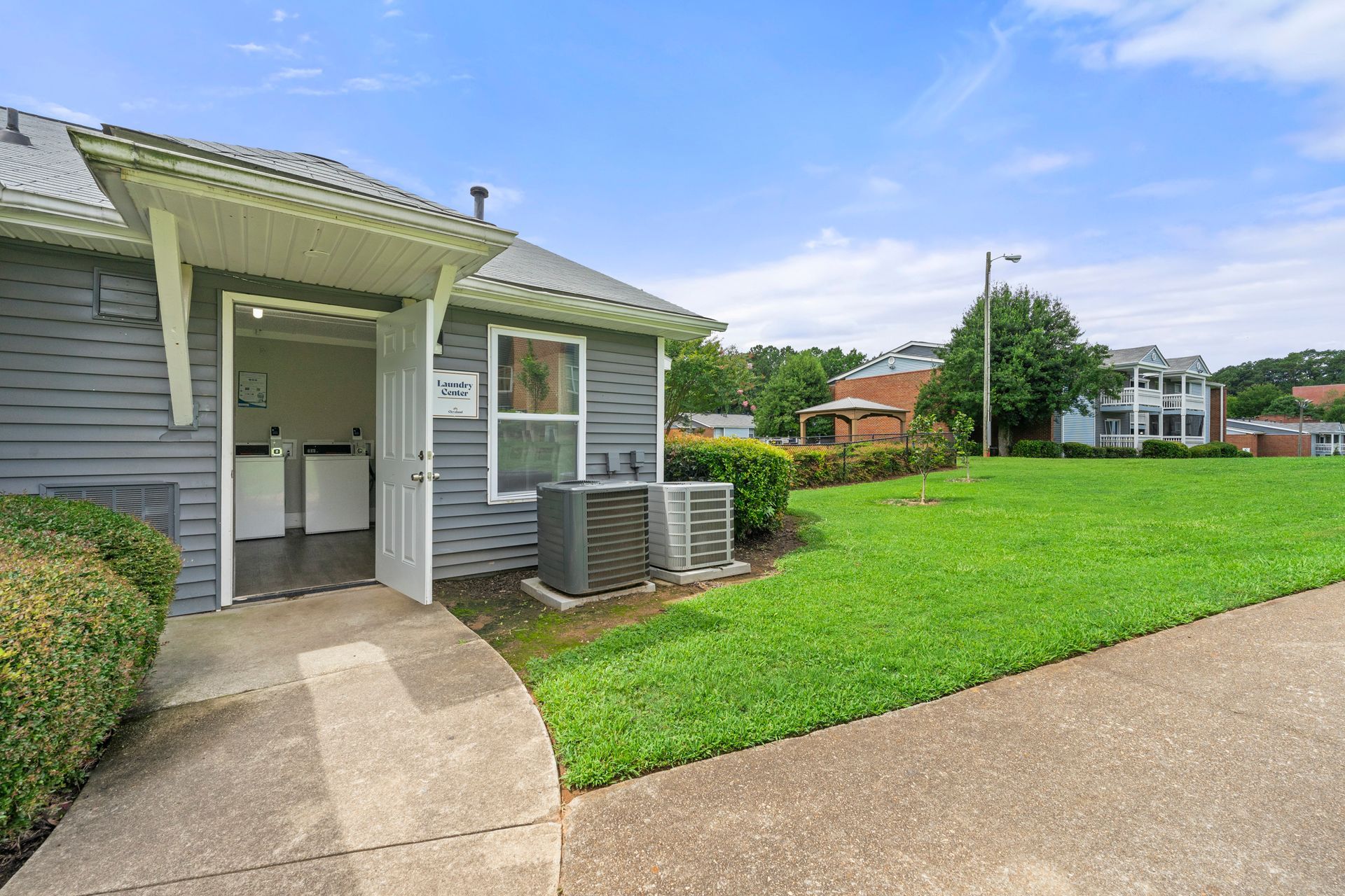 Exterior of a gray townhouse with a covered entry, green lawn, and paved walkway on a sunny day