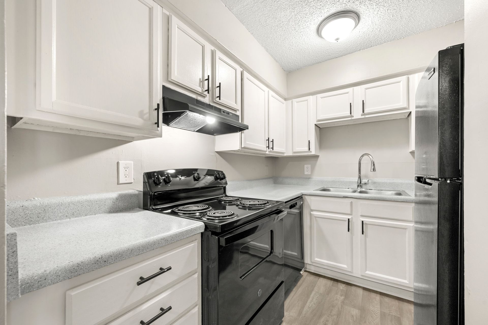 Bright white kitchen with black stove and fridge, white cabinets, and light gray countertops
