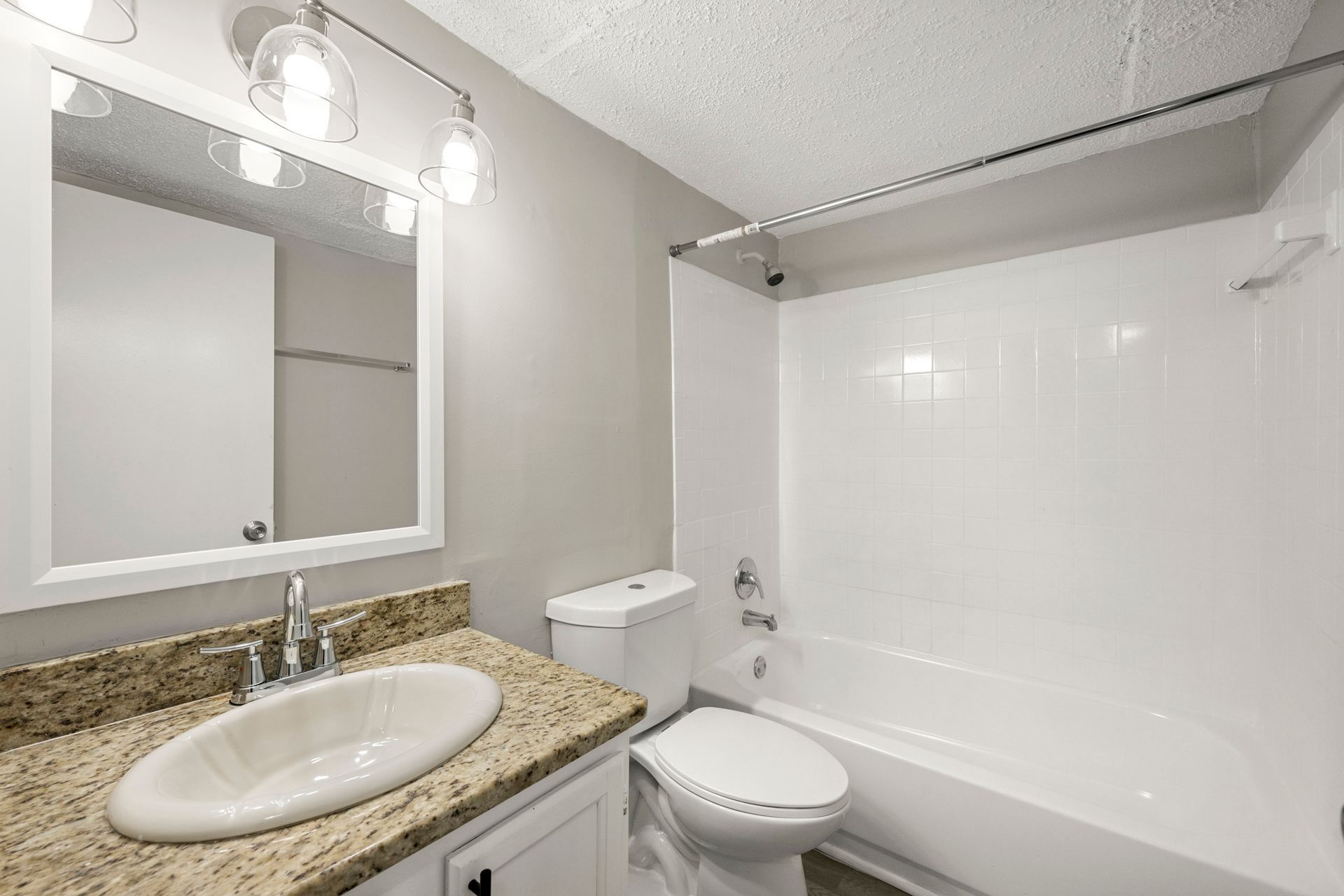 Bright bathroom with granite vanity, mirror lights, toilet, and white tub-shower combo