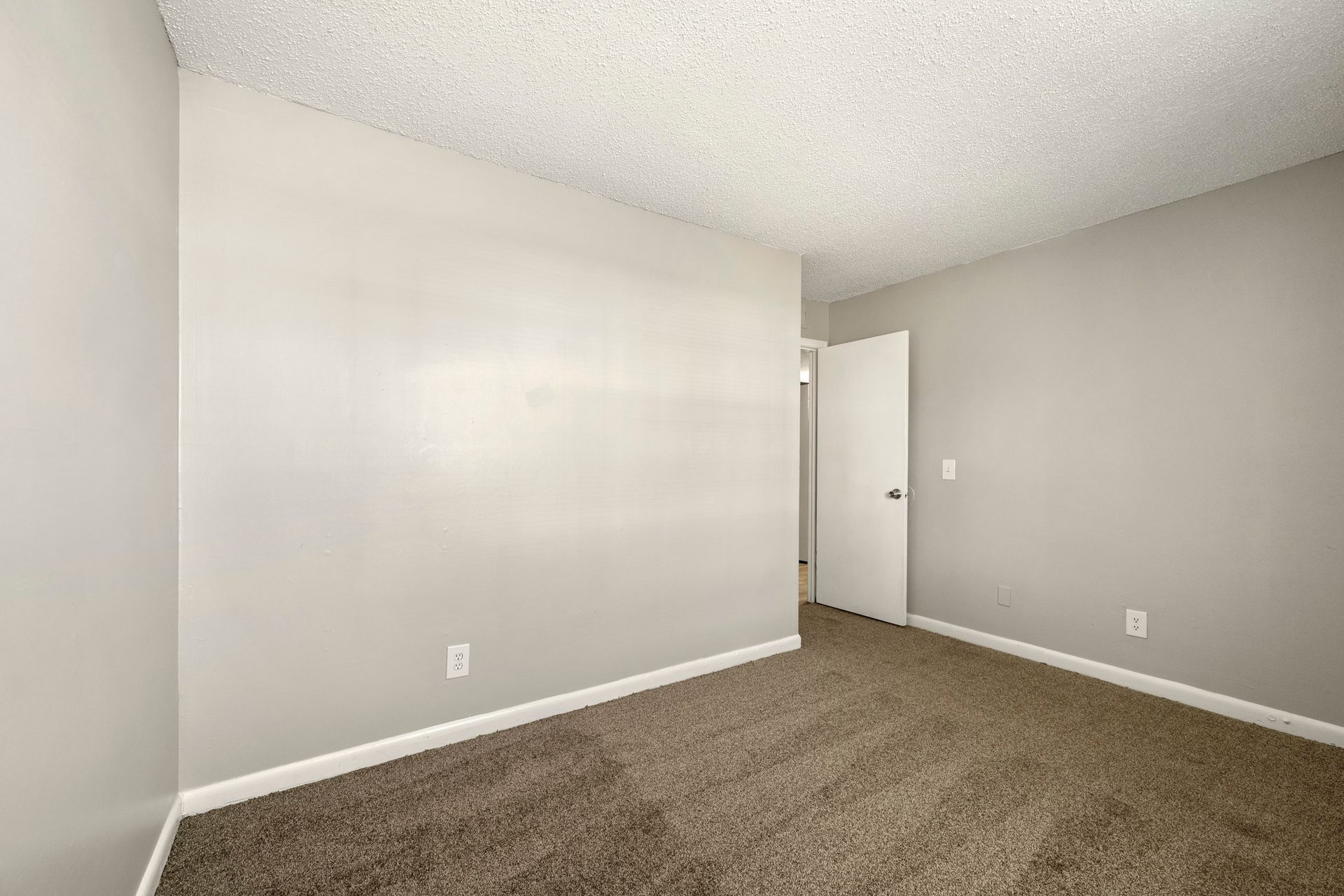 Empty beige bedroom with carpeted floor and white walls, viewed toward an open door.