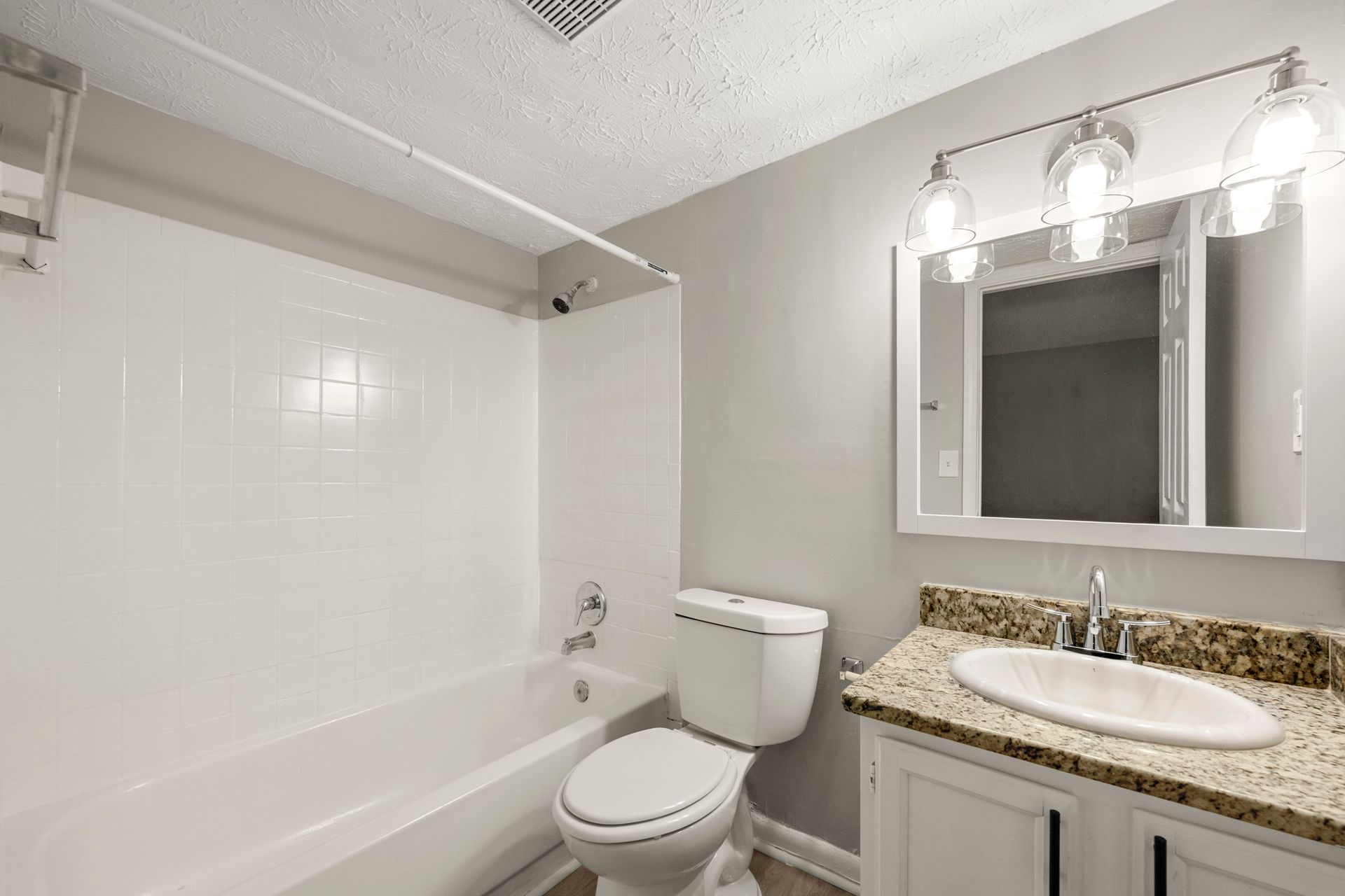 Bright bathroom with tub, toilet, vanity sink, mirror, and granite countertop.
