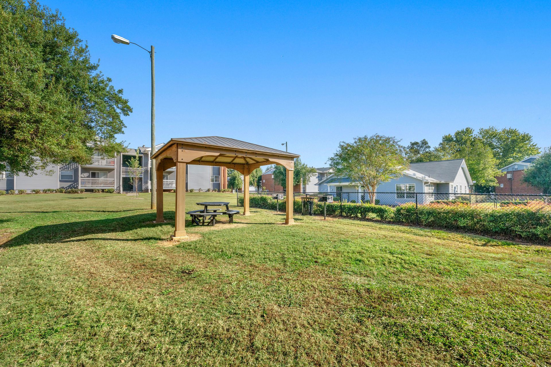 Park gazebo with picnic tables in a sunny green park under a blue sky
