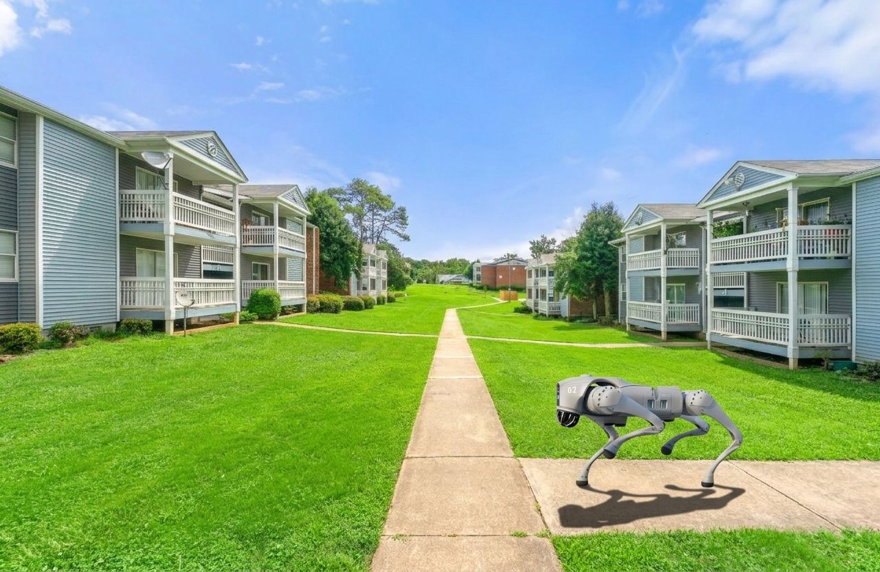 Covered picnic table in a grassy courtyard near apartment buildings and a brick wall