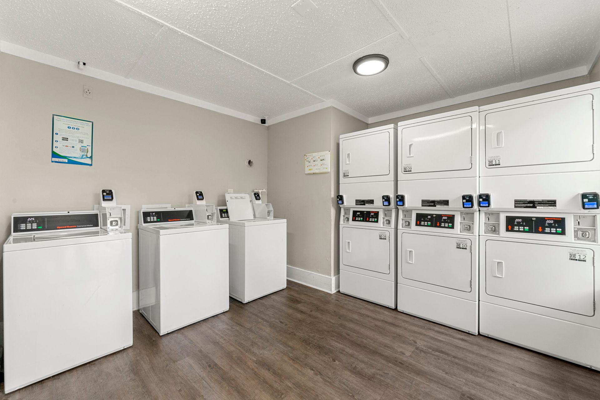 Bright laundry room with white washers and dryers on wood-look flooring.