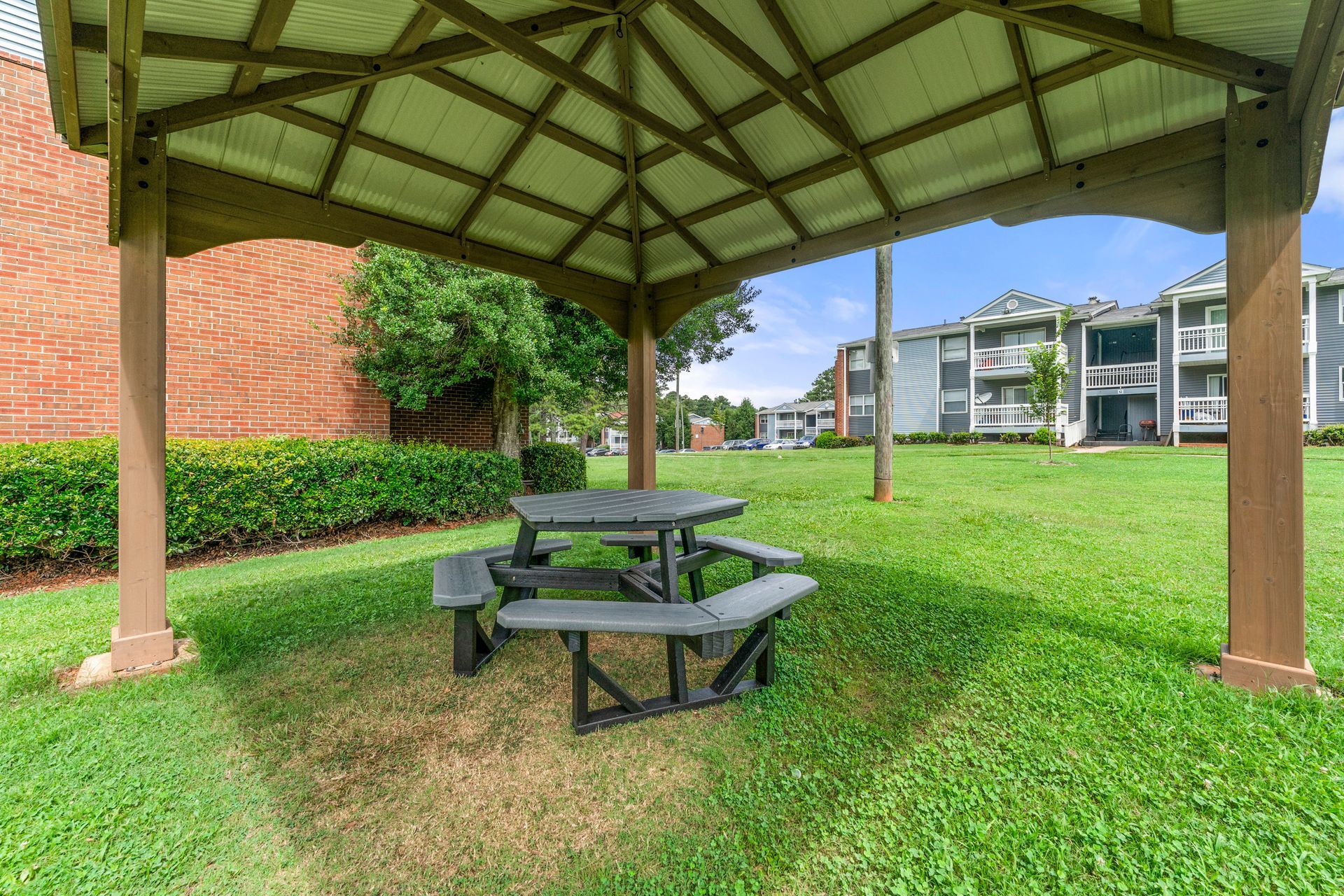 Covered picnic table in a grassy courtyard near apartment buildings and a brick wall