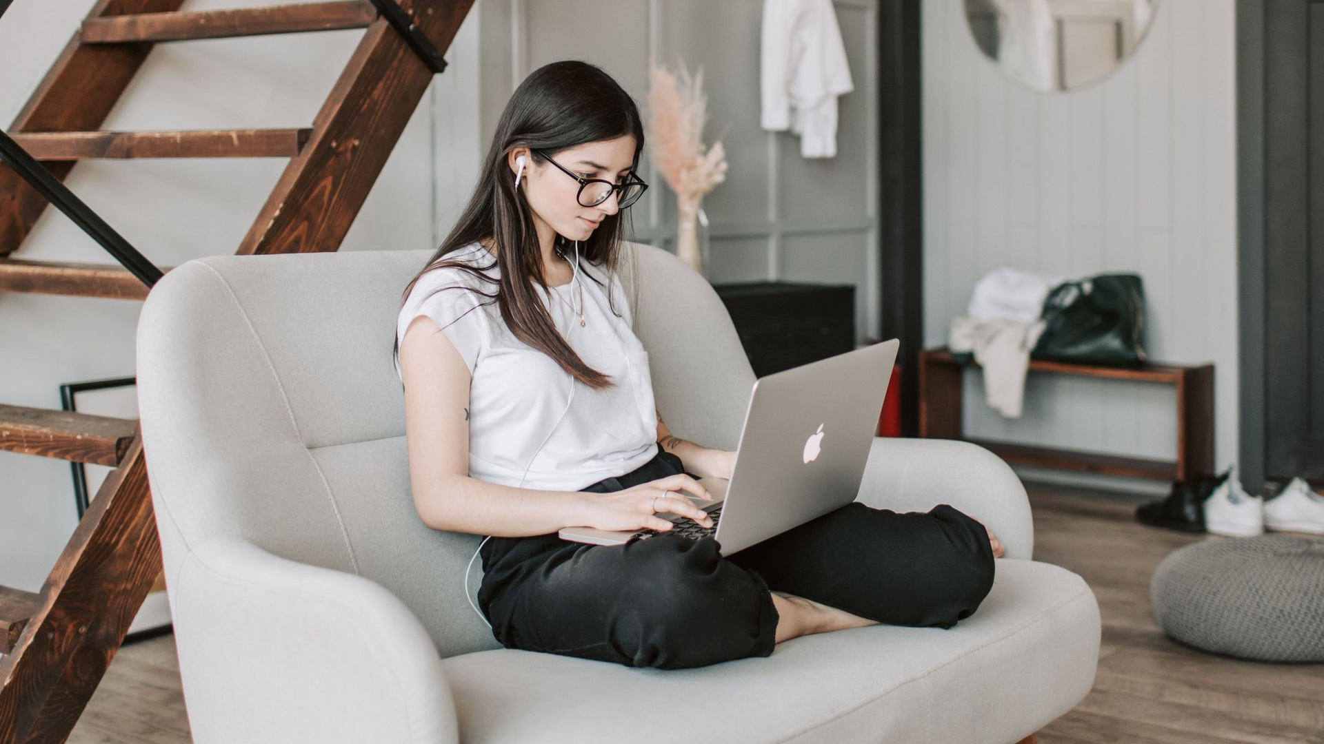 Woman sitting on a beige couch using a silver laptop in a bright living room