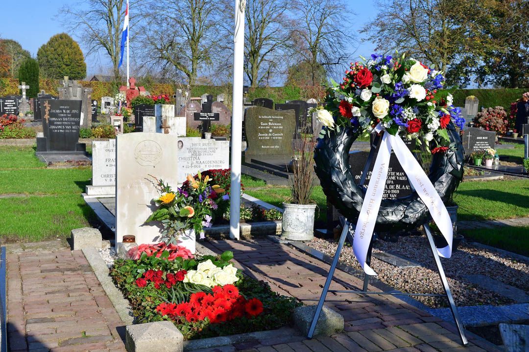 Een graf op een begraafplaats, versierd met een kleurrijke bloemenkrans op een standaard en verse bloemen op de grond.