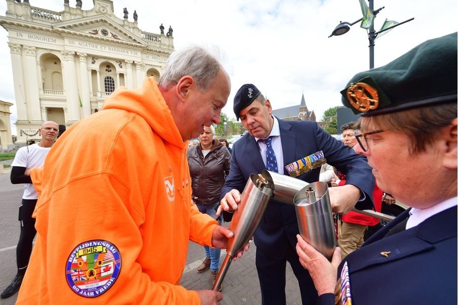 Drie mensen nemen deel aan een ceremoniële fakkelestafette voor een klassiek gebouw.