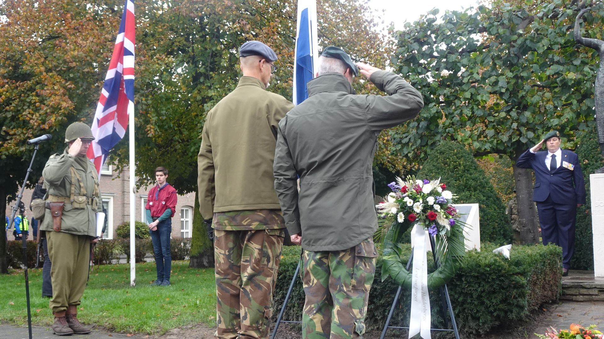 Tijdens een herdenkingsceremonie in de openlucht staan ​​verschillende mensen in militaire uniformen en met een krans bij een monument.