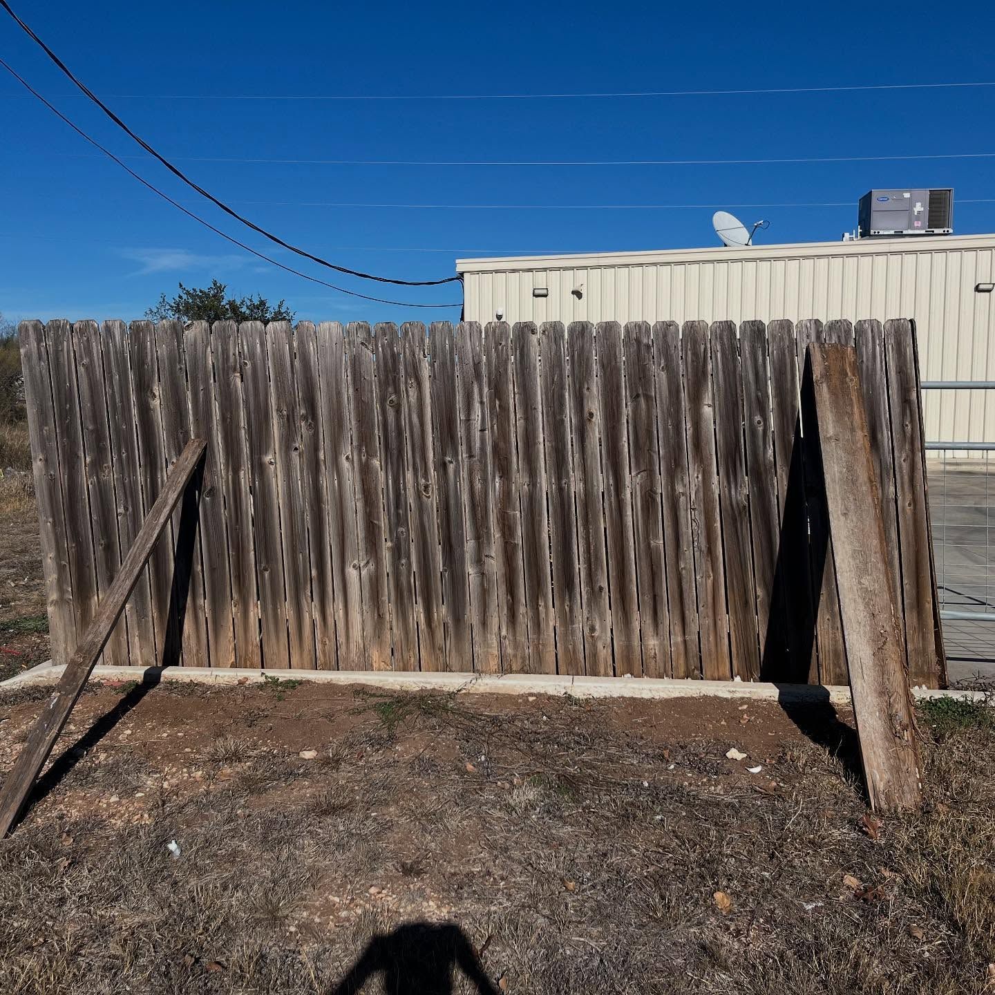 A weathered wooden fence stands outdoors under a clear blue sky, supported by two wooden braces.