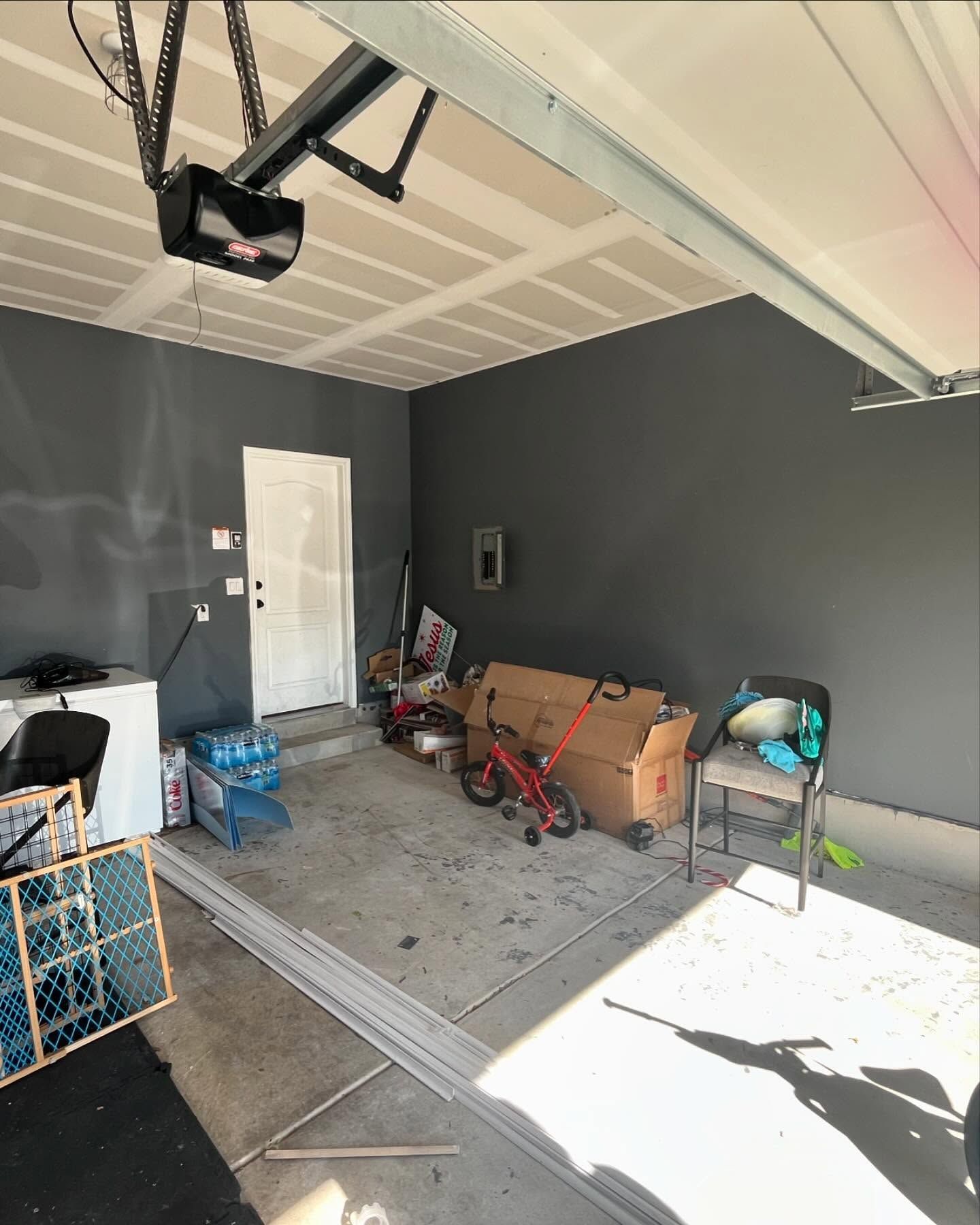 A garage interior with dark gray walls, a white door, a bicycle, cardboard boxes, and a chair on a concrete floor.
