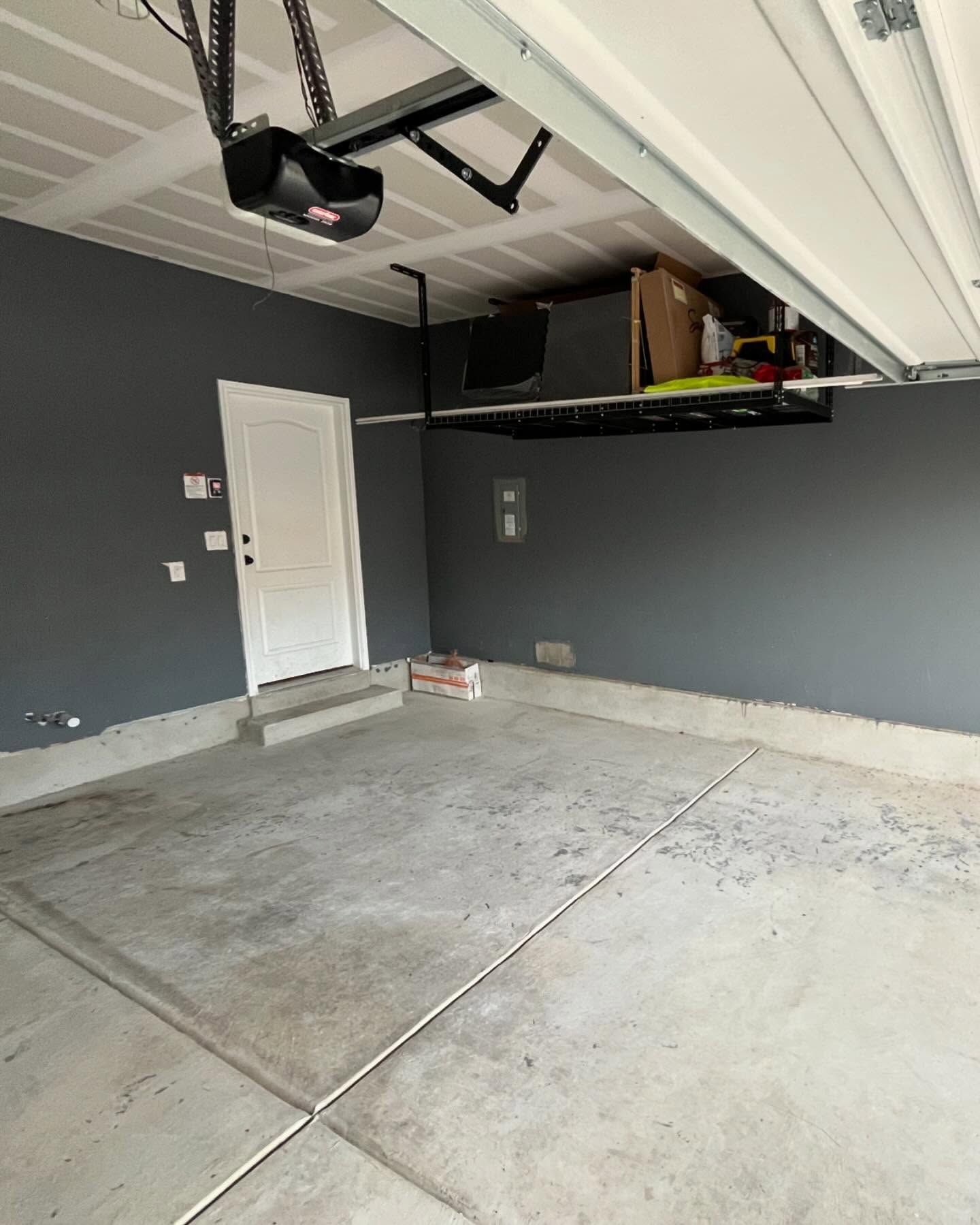 An interior view of a garage featuring gray walls, a white side door, a concrete floor, and overhead storage racks.