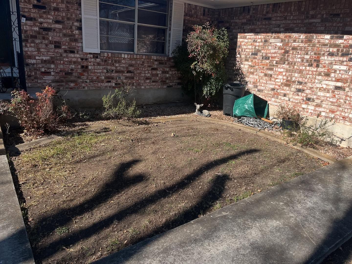 A brick house exterior with a patch of sparse, brown grass in the front yard and a small shrub by the foundation.