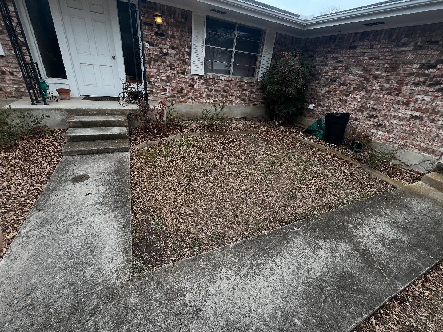 A brick house exterior with a white door, concrete steps, and a yard covered in fallen leaves.