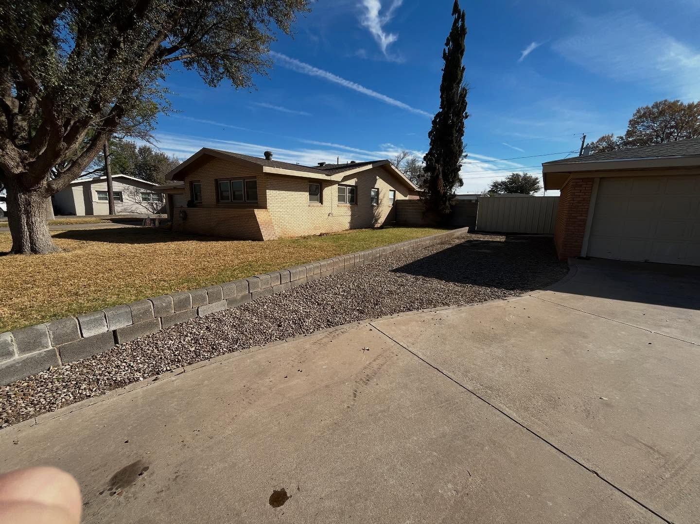 A beige house with a gravel front yard and a concrete driveway under a clear, sunny blue sky.