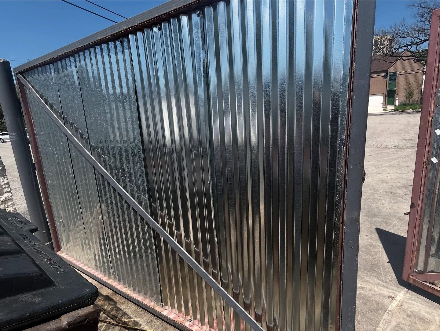 A large, rectangular gate frame with shiny corrugated metal panels, featuring a diagonal steel support brace.