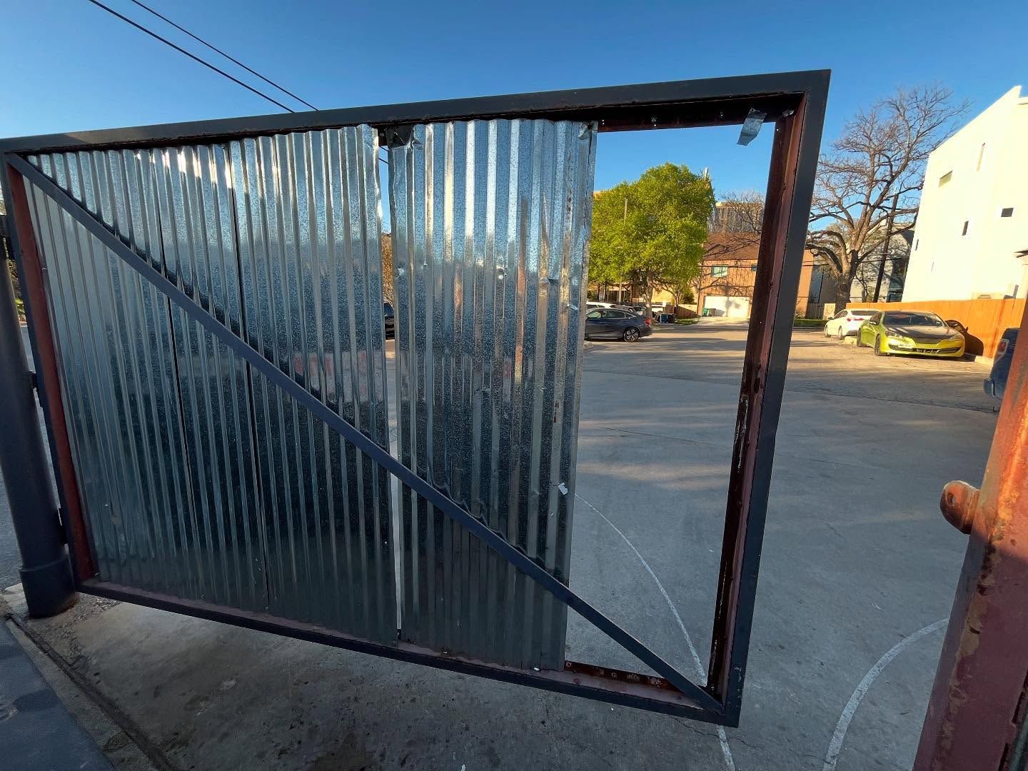 A rectangular gate frame featuring corrugated metal panels covers the left side, opening to a parking lot at sunset.
