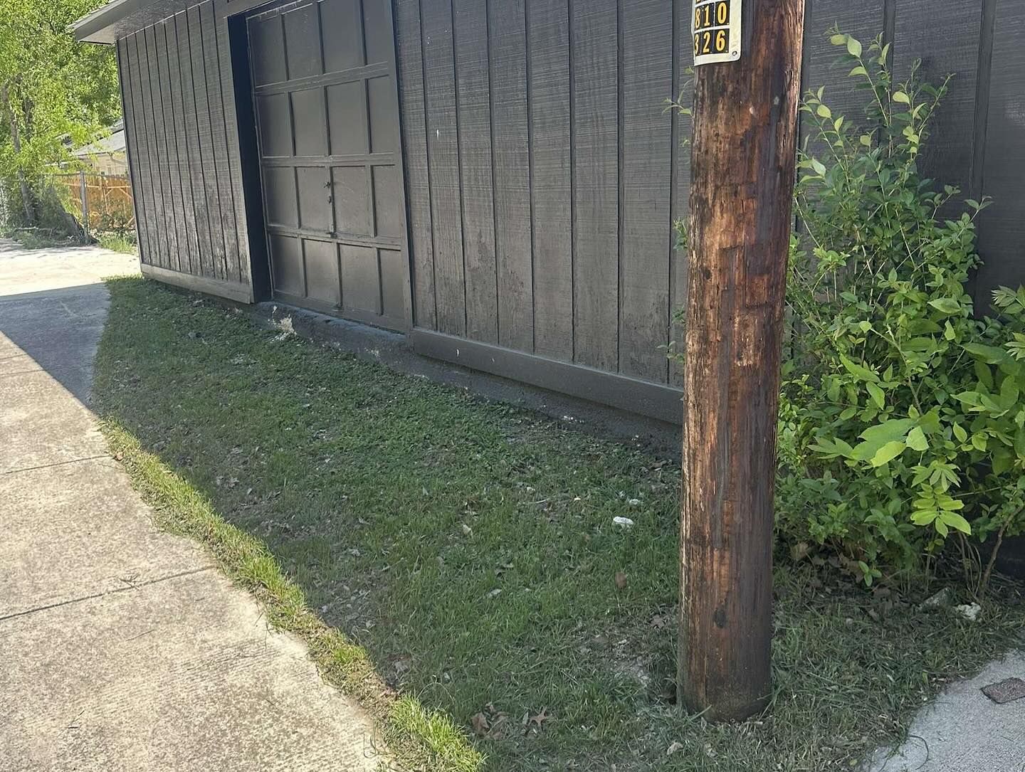 A dark wooden fence with a latticed section stands beside a patch of grass, a utility pole, and a sidewalk.