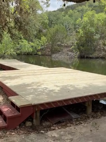 Wooden dock beside a calm river, surrounded by dense green trees.