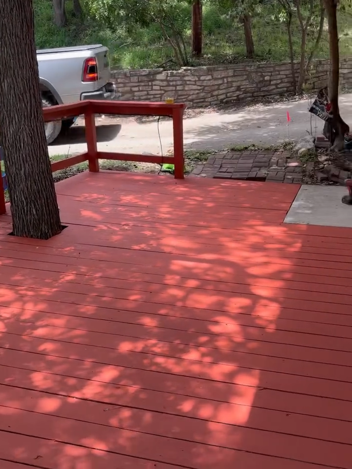 Red wooden deck beside a tree, stone wall, and parked silver truck in the background.