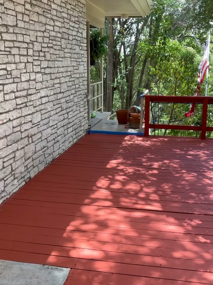 Red deck beside a stone wall, overlooking trees and a railing in dappled sunlight.