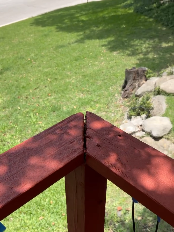 Red wooden railing corner overlooking a green lawn and rocks in a backyard