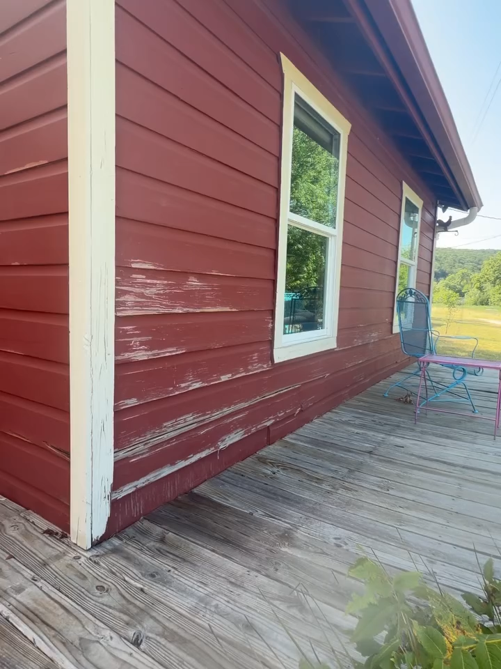 Red wooden house exterior with white trim and a window, showing a weathered deck in front.