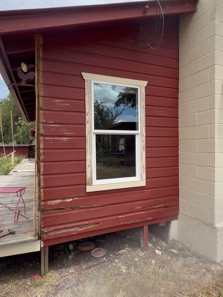 Small red wooden house wall with a white-framed window beside a beige brick wall.
