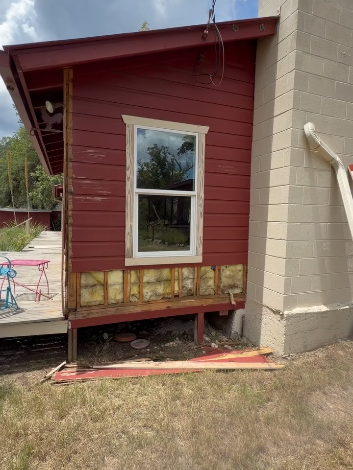 Red-sided building corner with a window, beige siding, and exposed foundation under construction.