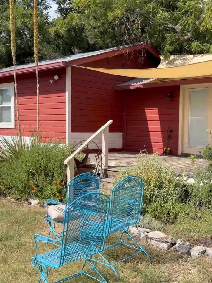 Red house with white-trimmed door and windows, blue metal patio chairs in the foreground, and a small ramp by the porch.