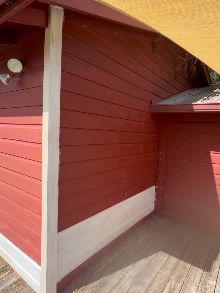 Red wooden building corner with white trim and a covered porch area