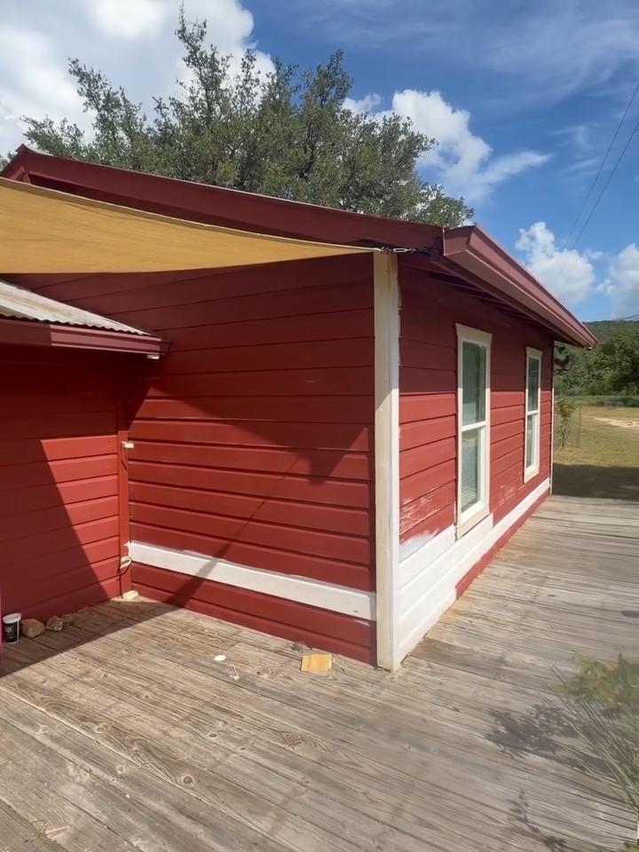 Red house exterior with white trim and wooden deck under a blue sky