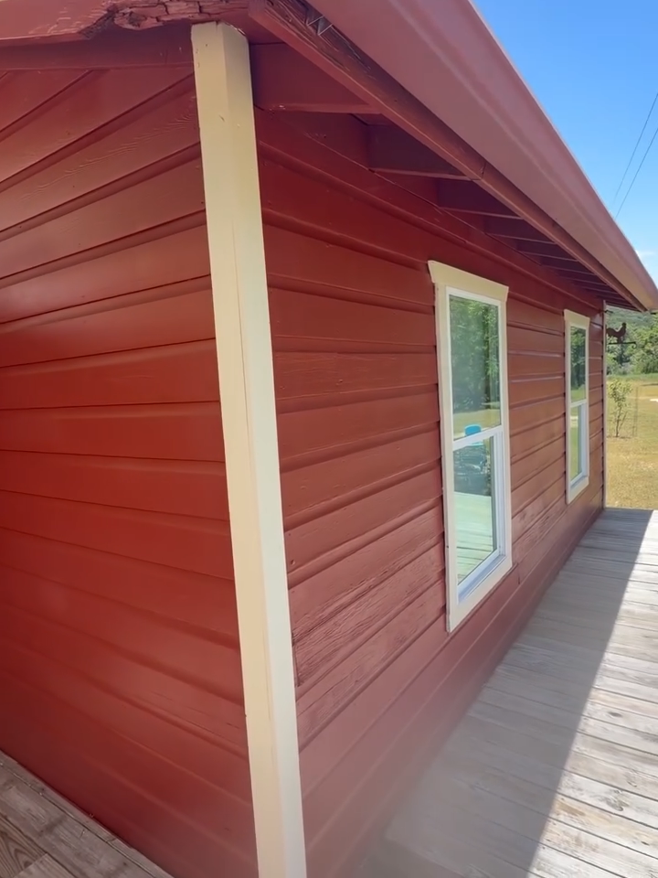 Red wooden house exterior with white trim and a side window, viewed along a deck walkway