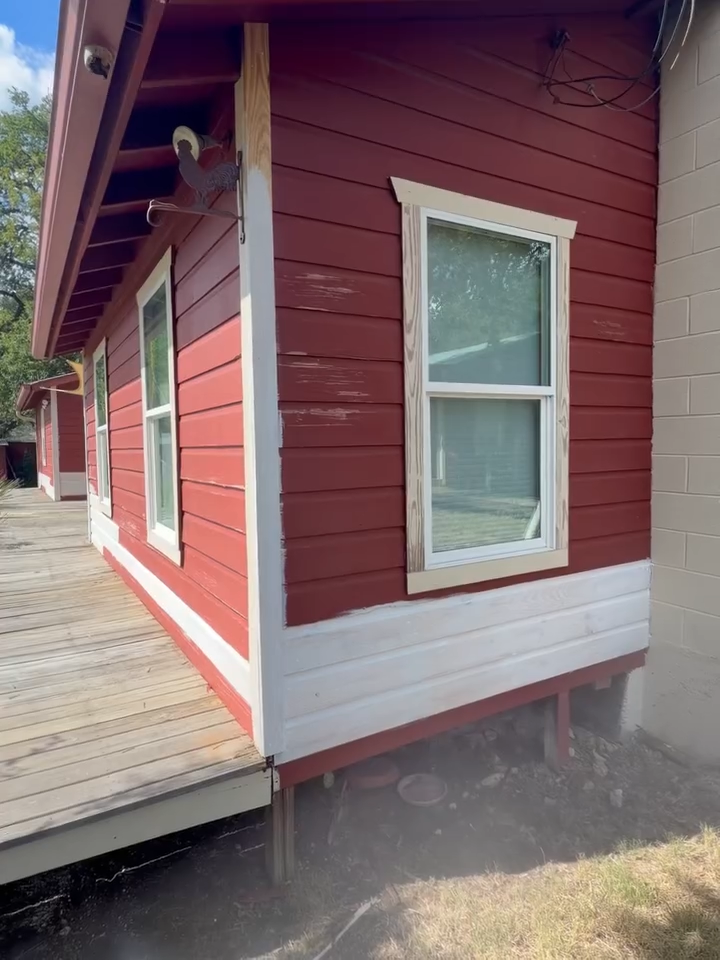 Red building corner with white-trimmed windows beside a wooden deck and gravel path