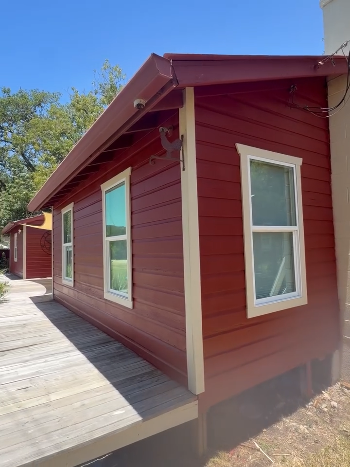 Red house with white-trimmed windows beside a wooden deck under a blue sky