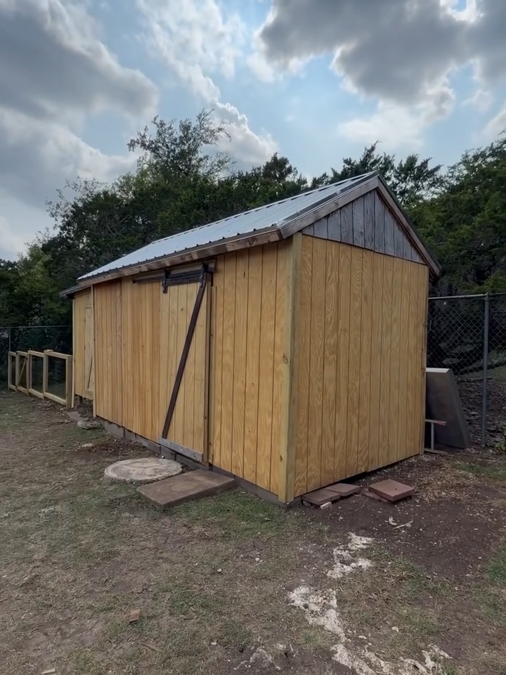 Small weathered wooden shed with a tin roof in a grassy yard under a cloudy sky
