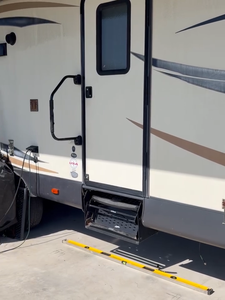 RV entrance with deployed wheelchair lift and black door, parked on concrete.